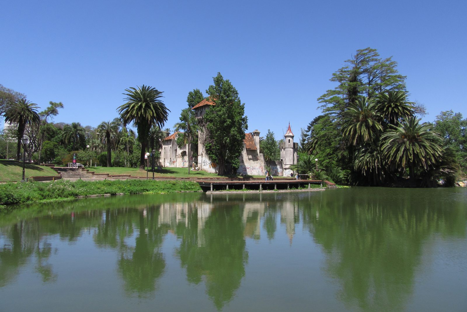 Lago del Parque Rodó con palmeras y el castillito reflejados en el agua, bajo un cielo despejado.