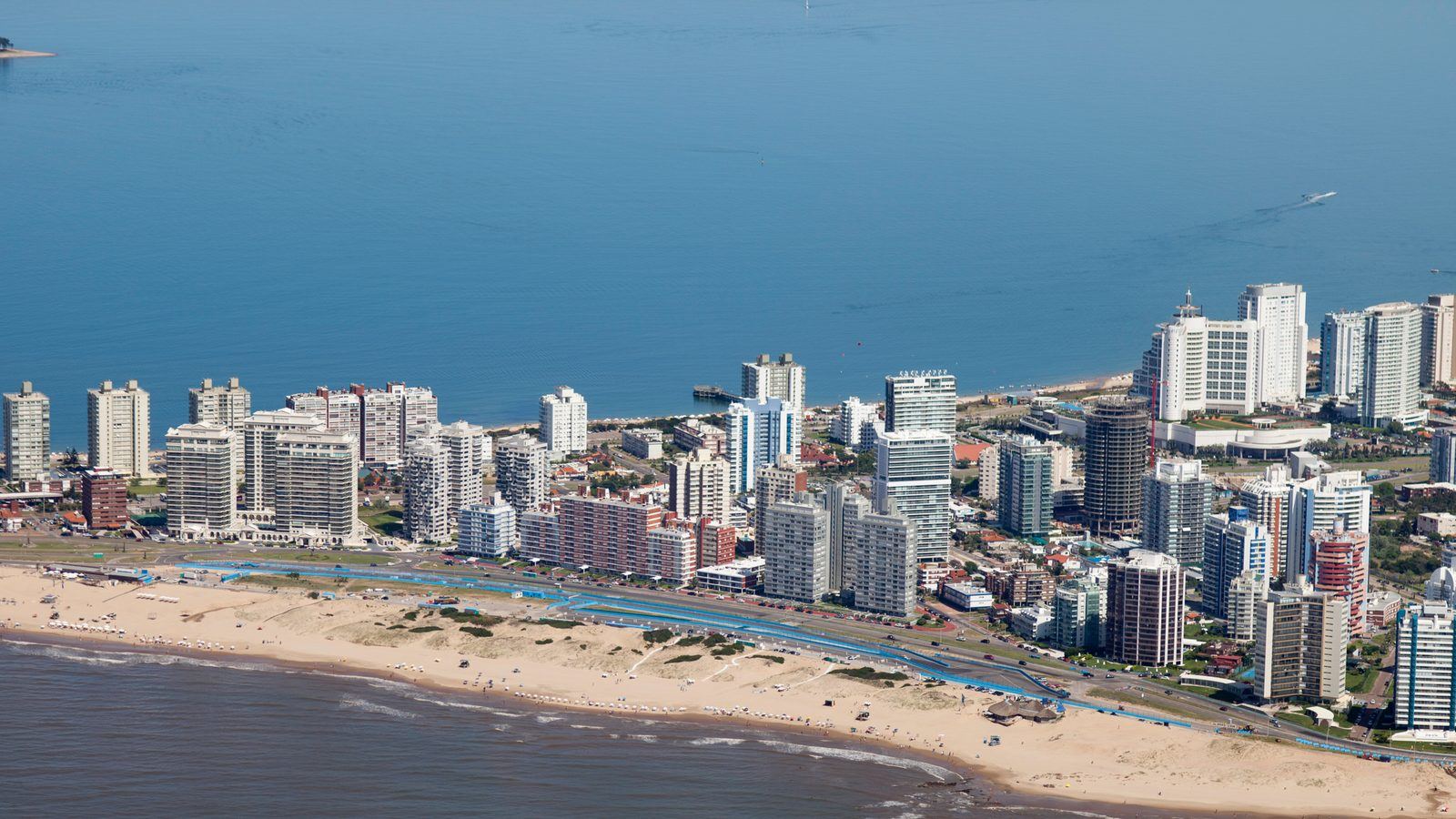 Vista aérea de Playa Brava y la base de la península de Punta del Este, con la línea de edificios frente al océano y la bahía de Playa Mansa al fondo.